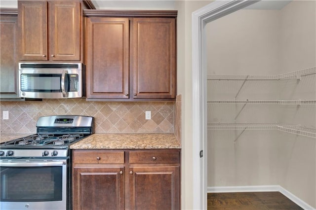 kitchen with appliances with stainless steel finishes, tasteful backsplash, baseboards, light stone counters, and dark wood-type flooring