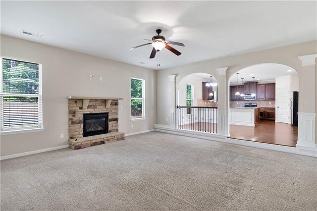 unfurnished living room with carpet floors, a ceiling fan, arched walkways, and visible vents