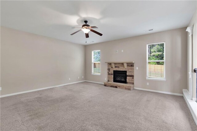 unfurnished living room featuring visible vents, plenty of natural light, ceiling fan, and a stone fireplace
