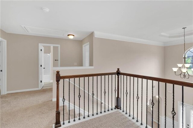corridor with crown molding, a chandelier, carpet, attic access, and baseboards