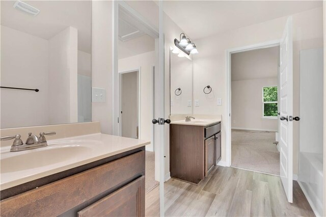 bathroom with visible vents, wood finished floors, two vanities, a sink, and baseboards
