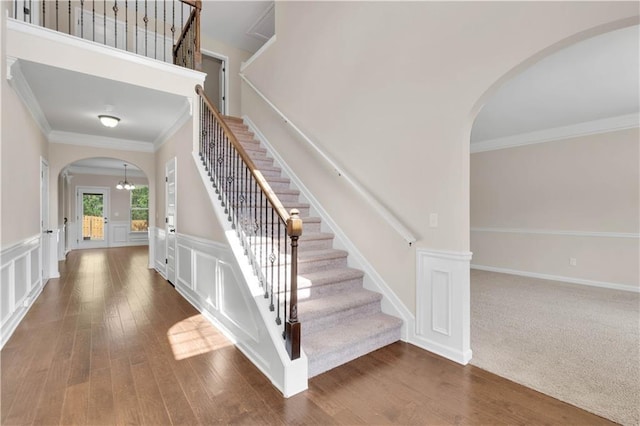stairs featuring arched walkways, ornamental molding, wainscoting, and wood finished floors