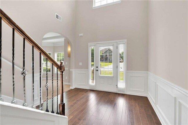 entryway with visible vents, arched walkways, stairway, a wainscoted wall, and dark wood-type flooring