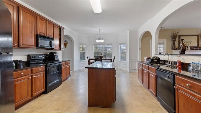 kitchen with a center island, black appliances, sink, hanging light fixtures, and dark stone counters