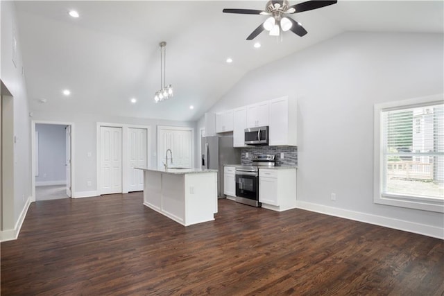 kitchen with white cabinets, appliances with stainless steel finishes, tasteful backsplash, hanging light fixtures, and a center island with sink