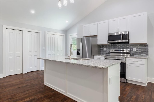 kitchen with appliances with stainless steel finishes, decorative backsplash, white cabinets, a center island with sink, and lofted ceiling