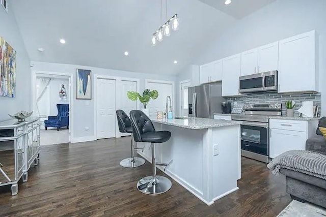 kitchen with white cabinets, appliances with stainless steel finishes, decorative light fixtures, decorative backsplash, and a kitchen island with sink