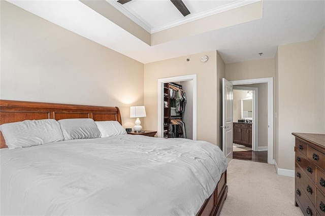 carpeted bedroom with ensuite bath, ceiling fan, a raised ceiling, a walk in closet, and a closet