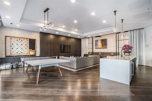 rec room with a tray ceiling, dark wood-style floors, a sink, and recessed lighting