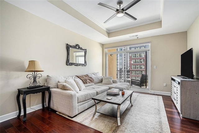 living room featuring ceiling fan, a raised ceiling, ornamental molding, and dark wood-type flooring