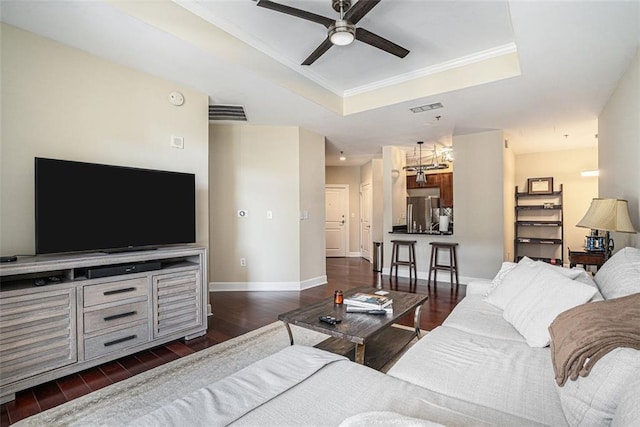 living room with a tray ceiling, ceiling fan, dark wood finished floors, baseboards, and crown molding