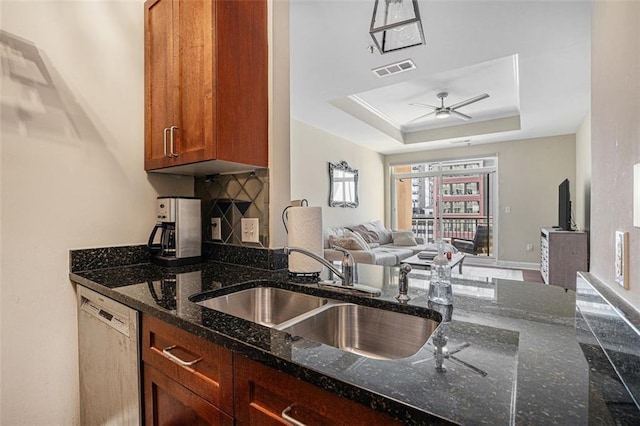 kitchen with stainless steel dishwasher, a sink, open floor plan, a ceiling fan, and dark stone counters