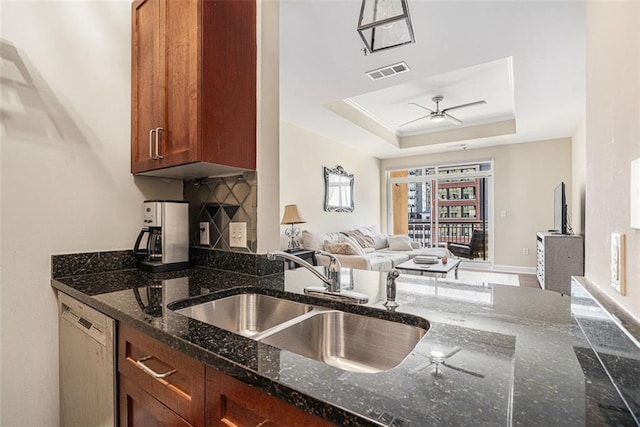 kitchen with dishwashing machine, a sink, open floor plan, ceiling fan, and dark stone counters