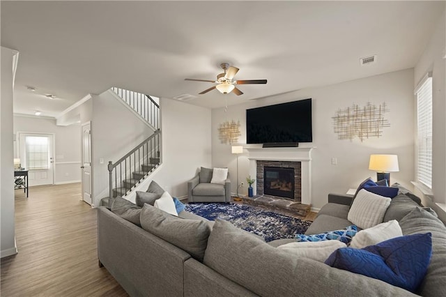 living room with ceiling fan, wood-type flooring, and a stone fireplace