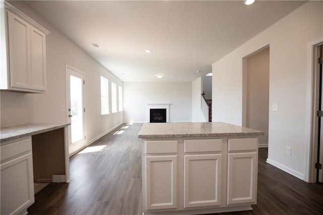 kitchen with dark hardwood / wood-style flooring, light stone countertops, a center island, and white cabinets