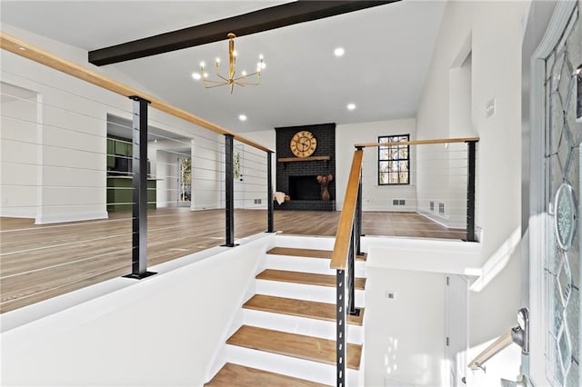 staircase with a fireplace, a chandelier, and beam ceiling