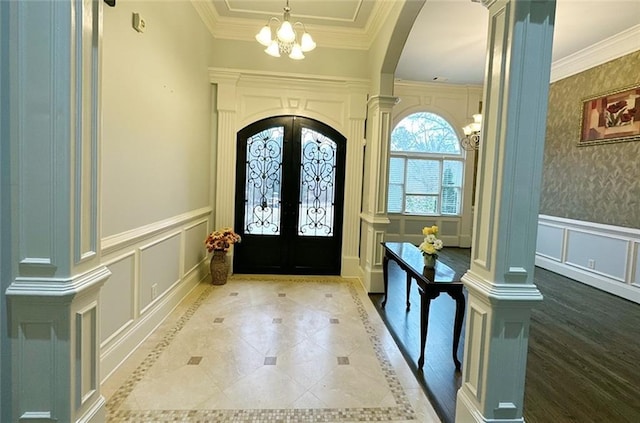 foyer entrance with decorative columns, french doors, a chandelier, and ornamental molding