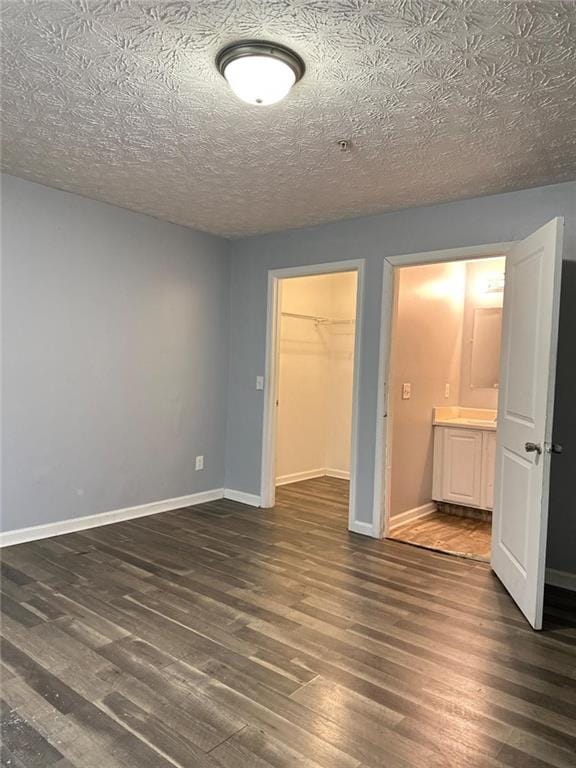 unfurnished bedroom with dark hardwood / wood-style flooring, a walk in closet, a textured ceiling, and a closet