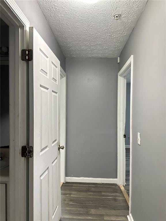 corridor with a textured ceiling and dark wood-type flooring