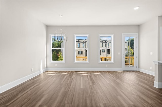 unfurnished dining area featuring baseboards, recessed lighting, wood finished floors, and a notable chandelier