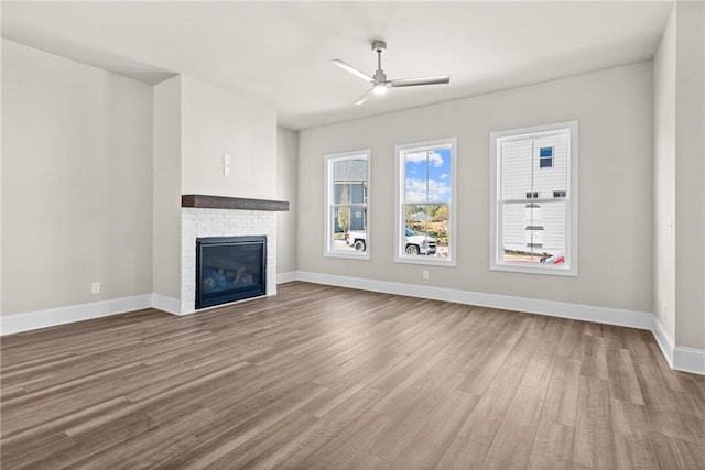 unfurnished living room with ceiling fan, wood finished floors, a glass covered fireplace, and baseboards