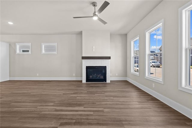 unfurnished living room featuring a healthy amount of sunlight, baseboards, wood finished floors, and a glass covered fireplace