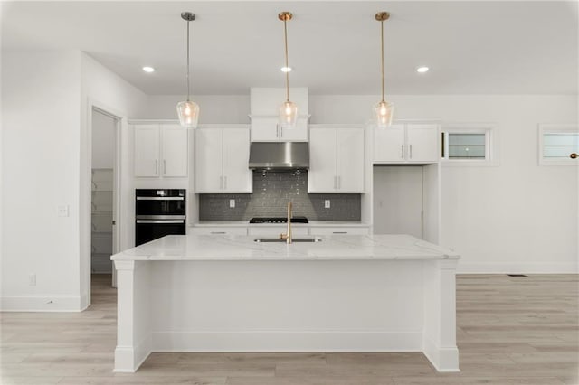 1937 Quarry Park Pl NW, Atlanta, GA 30318 - kitchen with under cabinet range hood, baseboards, white cabinetry, tasteful backsplash, and light wood-style floors