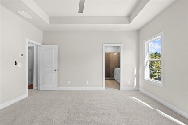 unfurnished bedroom featuring ensuite bathroom, a tray ceiling, light colored carpet, and baseboards