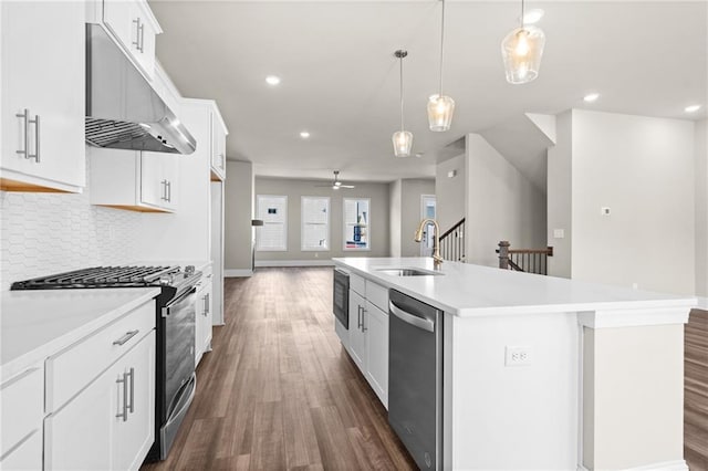 kitchen featuring a center island with sink, stainless steel appliances, decorative backsplash, dark wood-type flooring, and under cabinet range hood