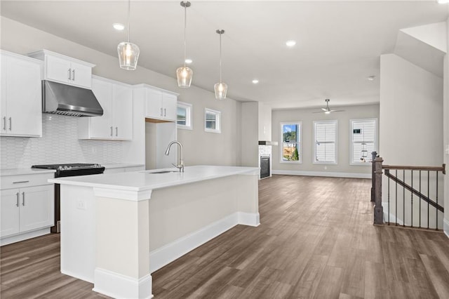 kitchen featuring under cabinet range hood, dark wood-style flooring, light countertops, backsplash, and an island with sink