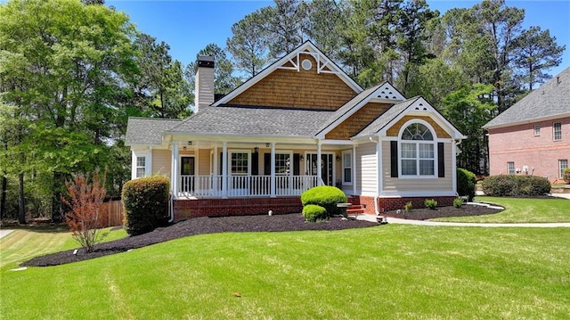 craftsman inspired home with a shingled roof, covered porch, a front yard, and a chimney
