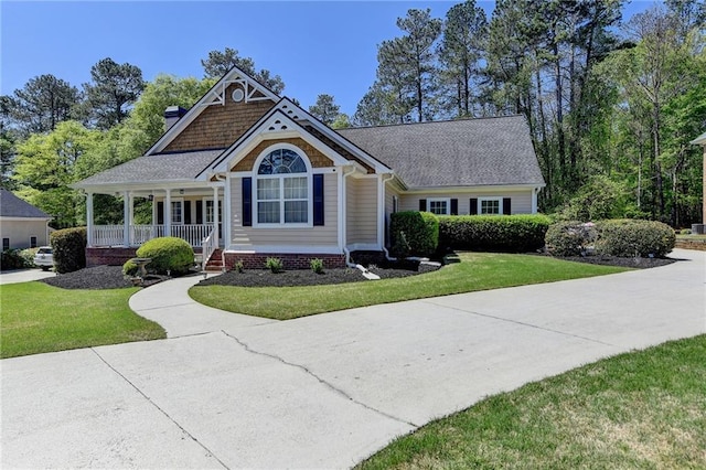 craftsman inspired home with a shingled roof, a porch, a chimney, and a front lawn