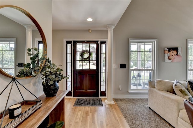 foyer entrance with light wood-style flooring, ornate columns, and plenty of natural light