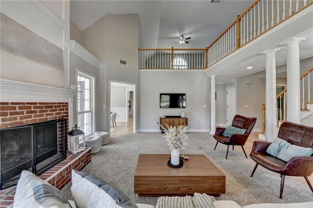 living room with a high ceiling, a brick fireplace, ornate columns, ceiling fan, and carpet