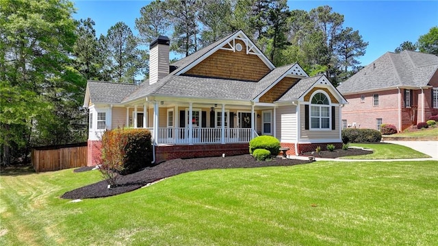 view of front facade featuring roof with shingles, covered porch, fence, and a front lawn