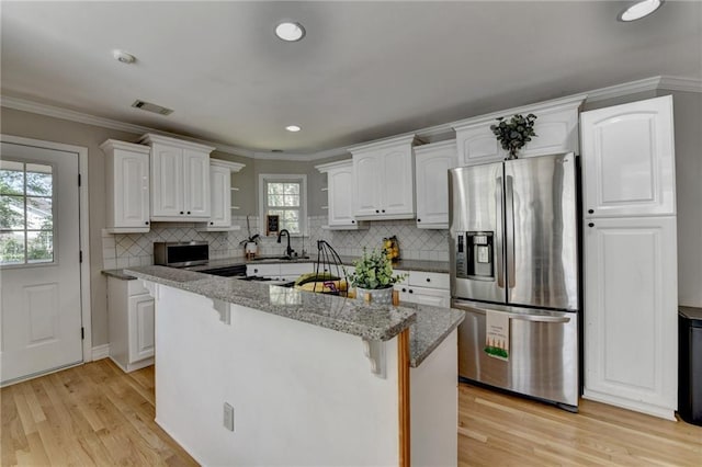 kitchen with light wood-type flooring, stainless steel fridge, white cabinets, visible vents, and a breakfast bar area