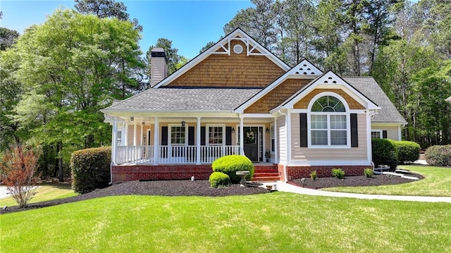 craftsman inspired home with roof with shingles, a chimney, covered porch, and a front yard