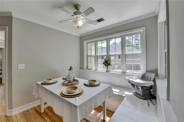 dining space with visible vents, baseboards, ornamental molding, a ceiling fan, and light wood-type flooring