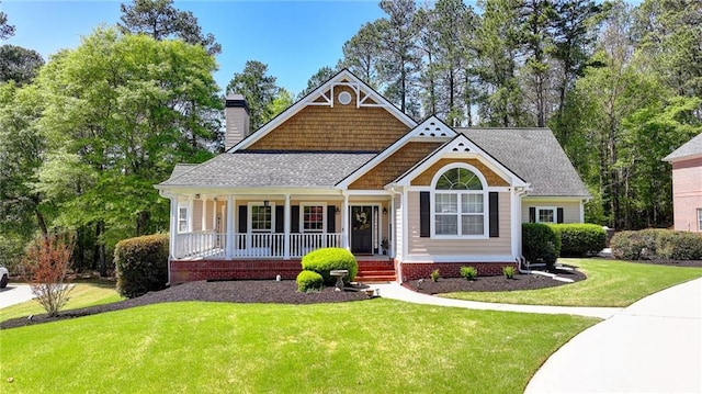 craftsman-style home with a porch, roof with shingles, a chimney, and a front yard