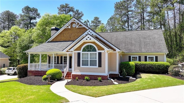 craftsman inspired home with a chimney, a front lawn, covered porch, and roof with shingles