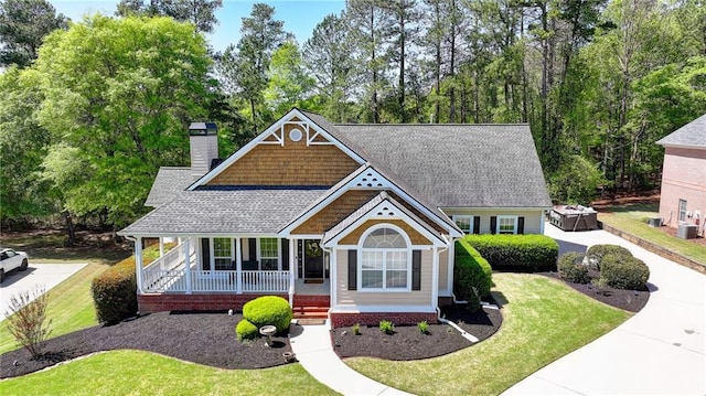 craftsman inspired home with a shingled roof, covered porch, a front yard, and a chimney