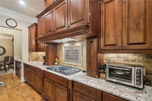 kitchen with ornamental molding, under cabinet range hood, decorative backsplash, stainless steel gas cooktop, and a toaster
