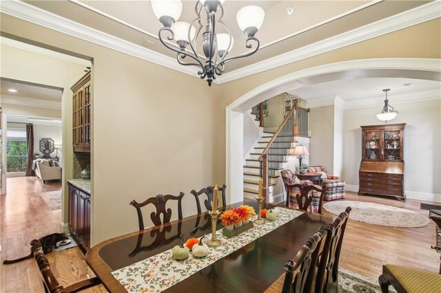 dining area with arched walkways, a notable chandelier, crown molding, stairway, and wood finished floors