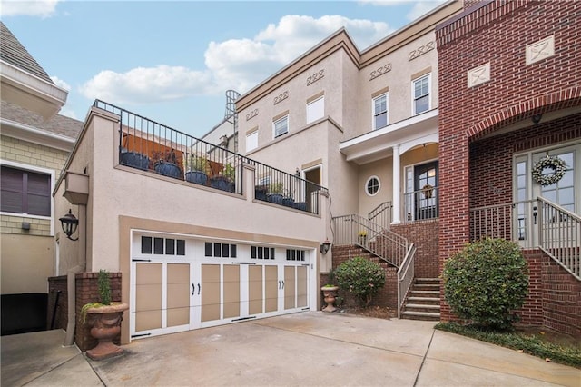 view of property with concrete driveway, an attached garage, stairway, and stucco siding
