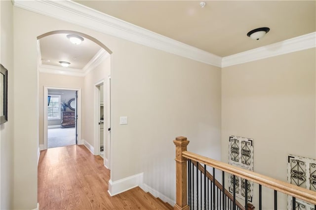 hallway featuring crown molding, light wood-style flooring, arched walkways, an upstairs landing, and baseboards