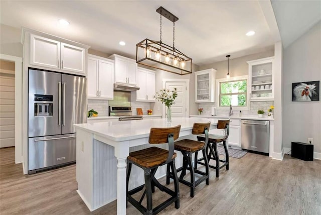 kitchen featuring a breakfast bar area, stainless steel appliances, white cabinets, a kitchen island, and decorative light fixtures