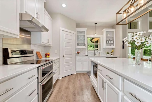 kitchen with sink, light wood-type flooring, double oven range, pendant lighting, and white cabinets