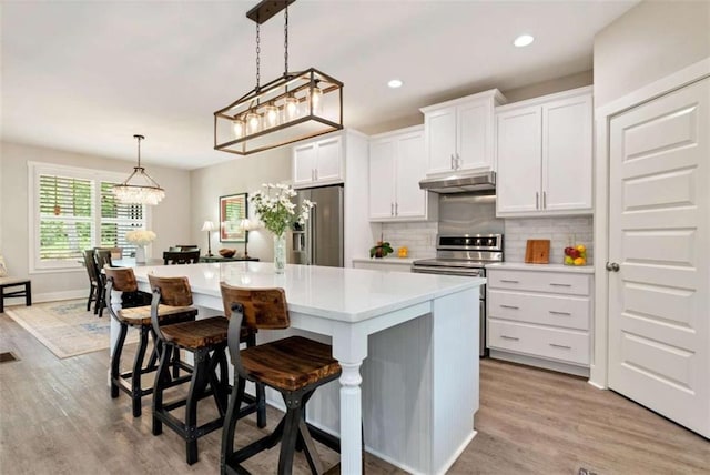 kitchen featuring a breakfast bar, white cabinetry, hanging light fixtures, stainless steel appliances, and a center island