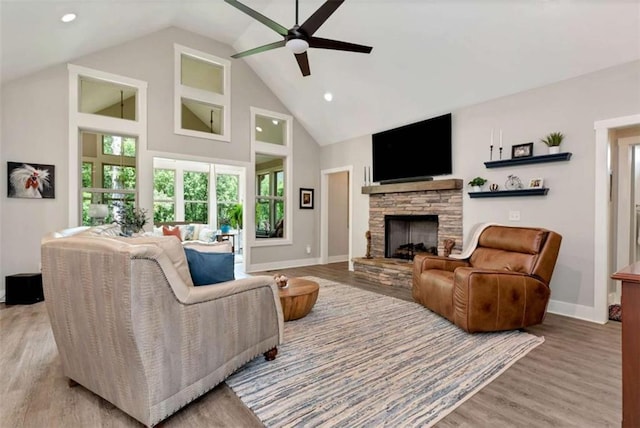 living room featuring ceiling fan, a stone fireplace, high vaulted ceiling, and light wood-type flooring