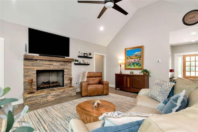 living room with ceiling fan, a stone fireplace, high vaulted ceiling, and light wood-type flooring